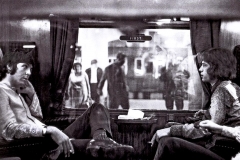 Paul McCartney (The Beatles) and Mick Jagger (The Rolling Stones) are travelling across the table from each other on a train at Euston Station